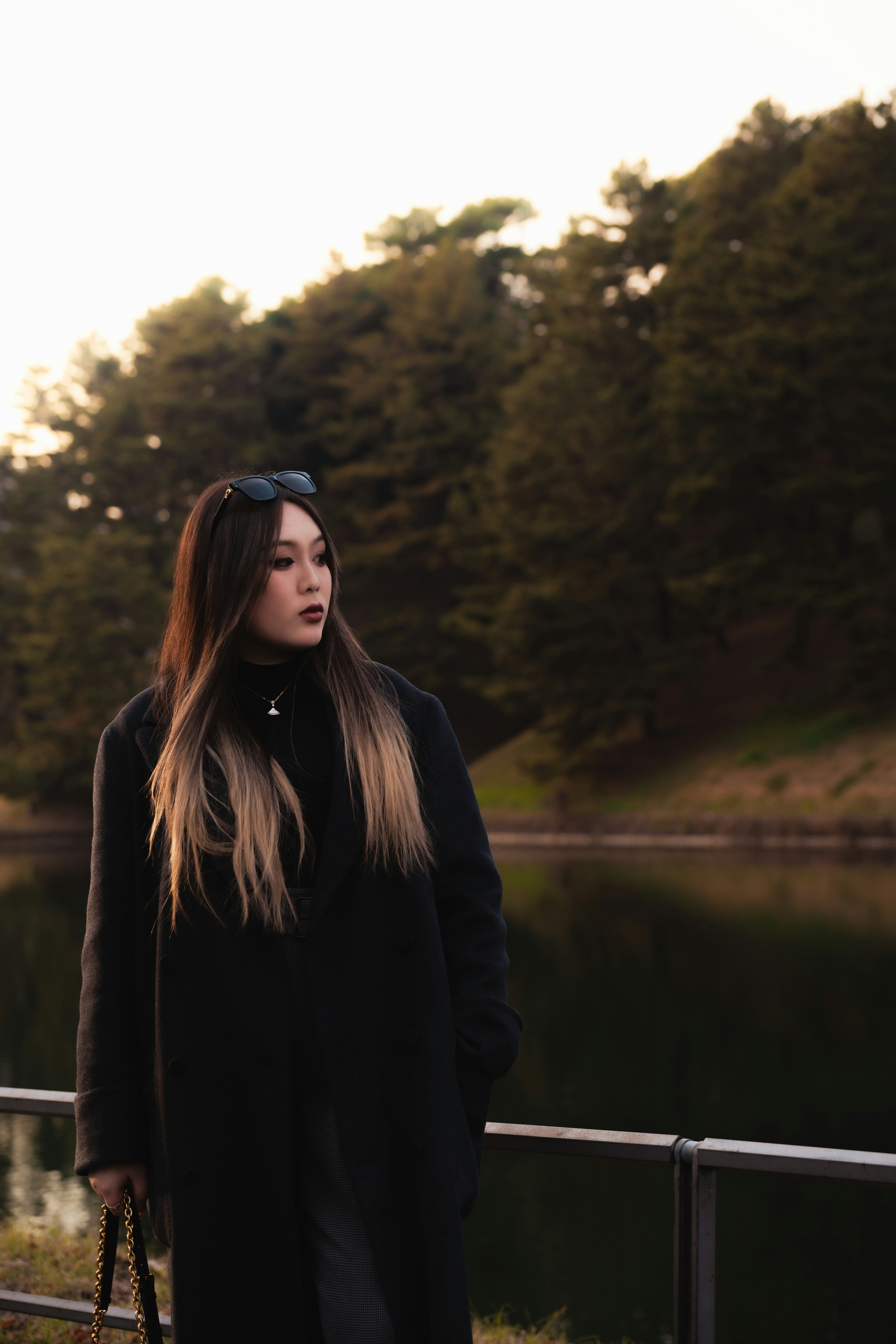 검은 코트를 입은 여자가 호수 근처에 서 있습니다