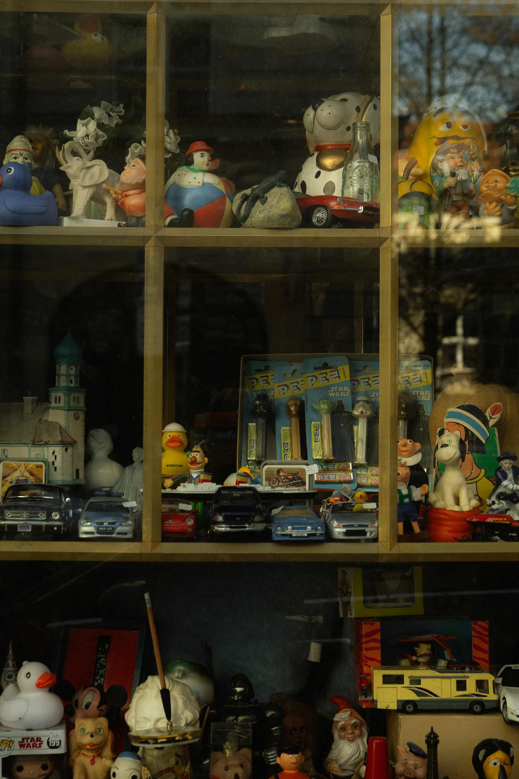A wooden cabinet with carded Pez dispensers standing behind glass, among toy cars and figurines