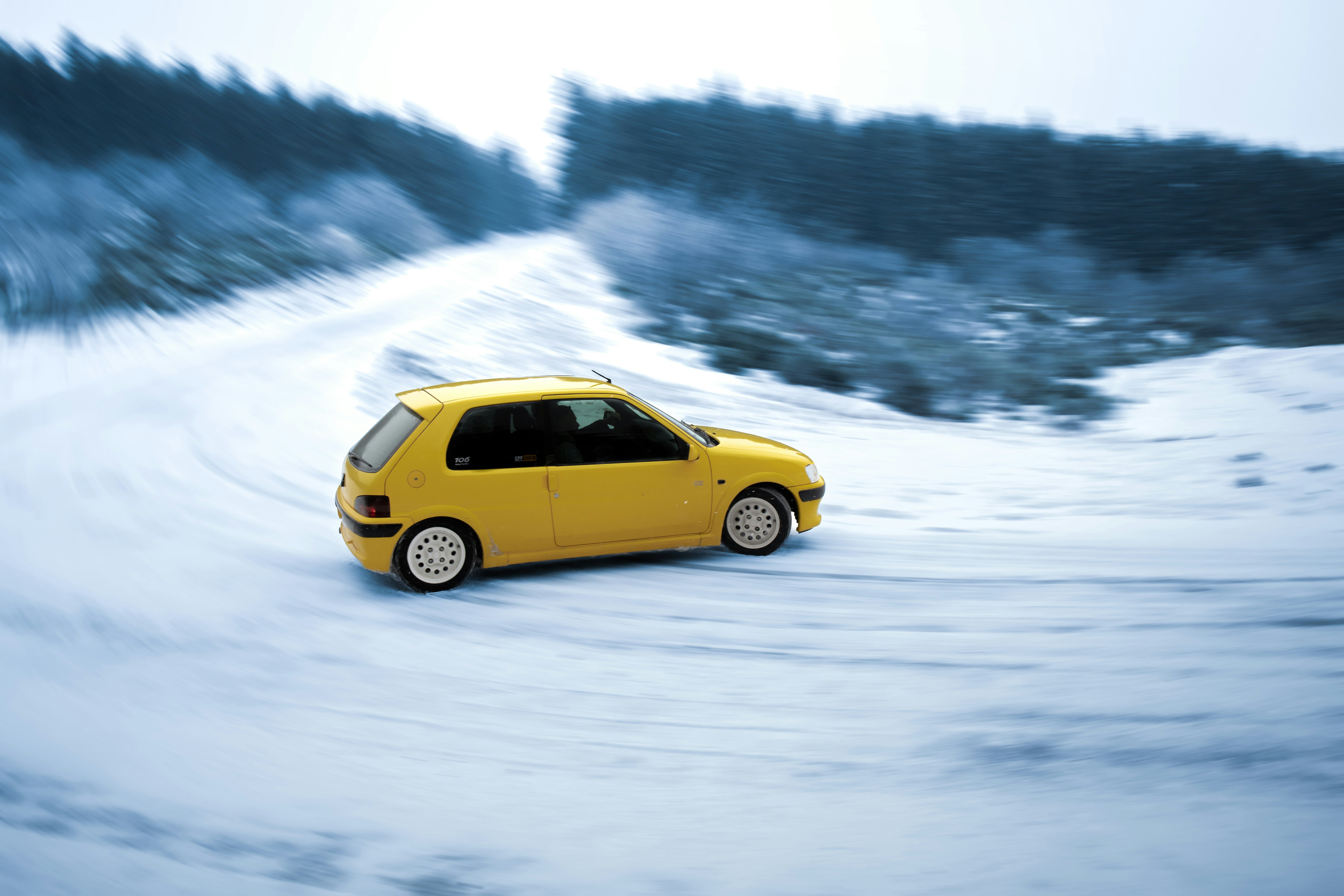 A small yellow car driving down a snow covered road