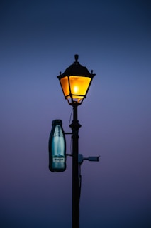 A lamp post with a bottle hanging from it's side