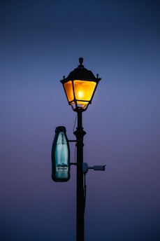 A lamp post with a bottle hanging from it's side
