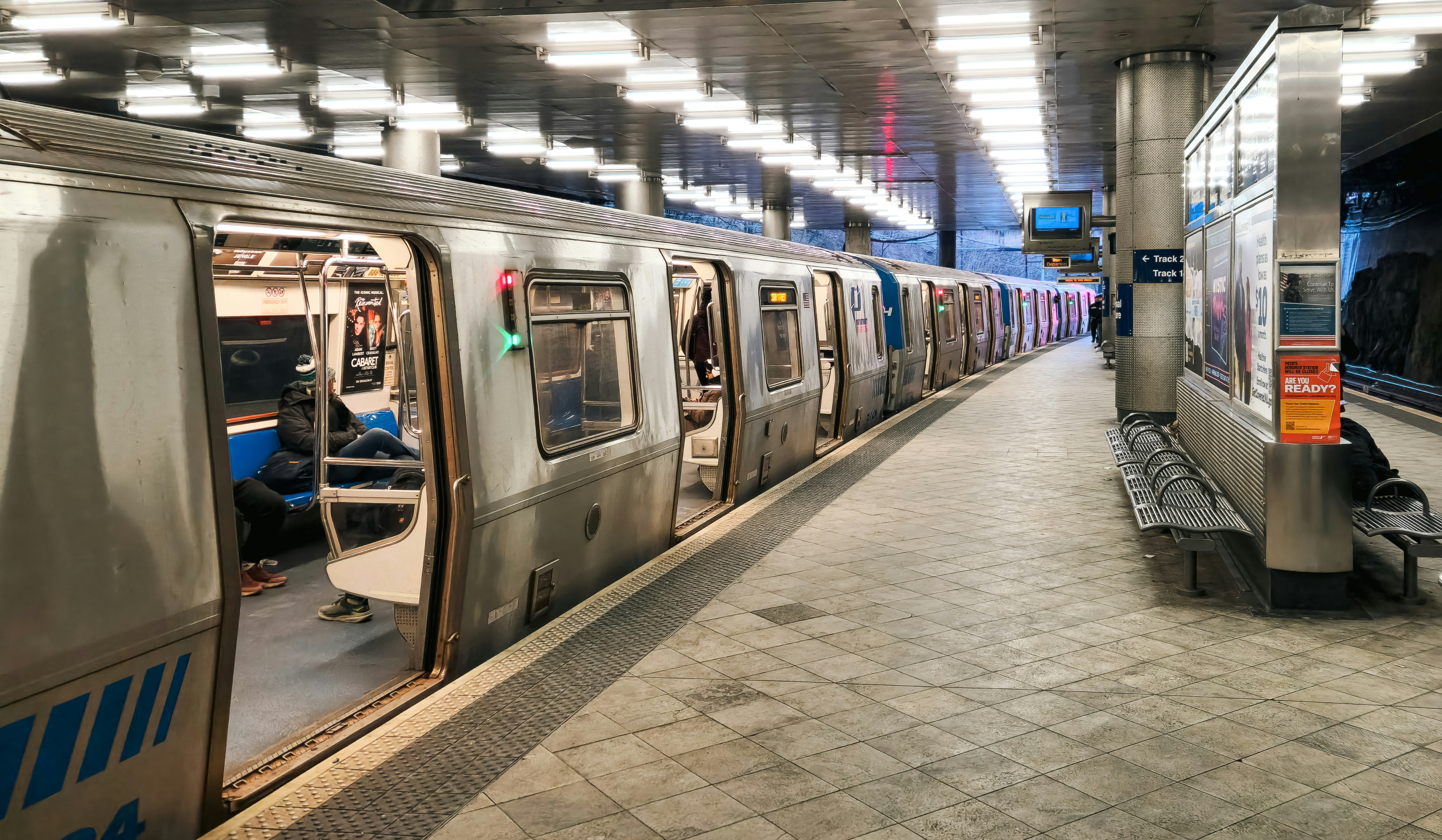 A PATH train is parked at the Journal Square station in Jersey City, New Jersey. Part of the Port Authority Trans-Hudson (PATH) system, this train connects New Jersey with New York City, serving as a crucial transit link for daily commuters. The station, a major transportation hub, features multiple platforms and modern infrastructure. The image captures the train’s blue and white exterior, platform details, and the urban transit atmosphere of one of the busiest stations in the region.
