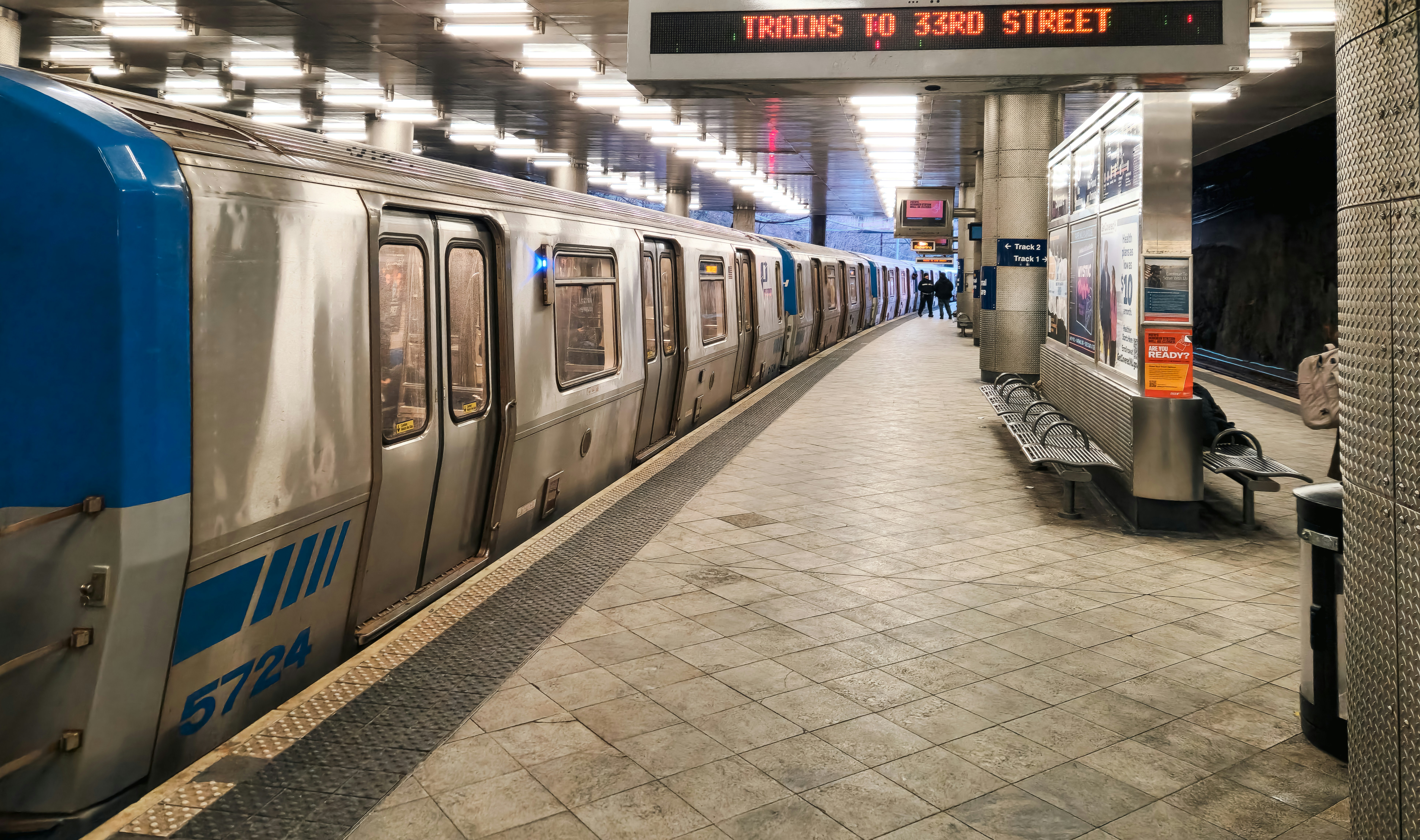 A PATH train is parked at the Journal Square station in Jersey City, New Jersey. Part of the Port Authority Trans-Hudson (PATH) system, this train connects New Jersey with New York City, serving as a crucial transit link for daily commuters. The station, a major transportation hub, features multiple platforms and modern infrastructure. The image captures the train’s blue and white exterior, platform details, and the urban transit atmosphere of one of the busiest stations in the region.