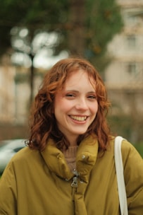 A woman with red hair is smiling and holding a white bag