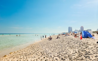 A beach filled with lots of people under a blue sky