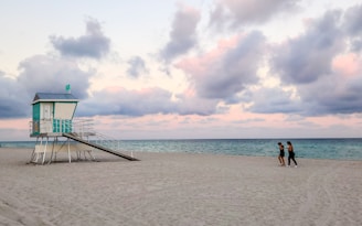 Two people walking on a beach near a lifeguard tower