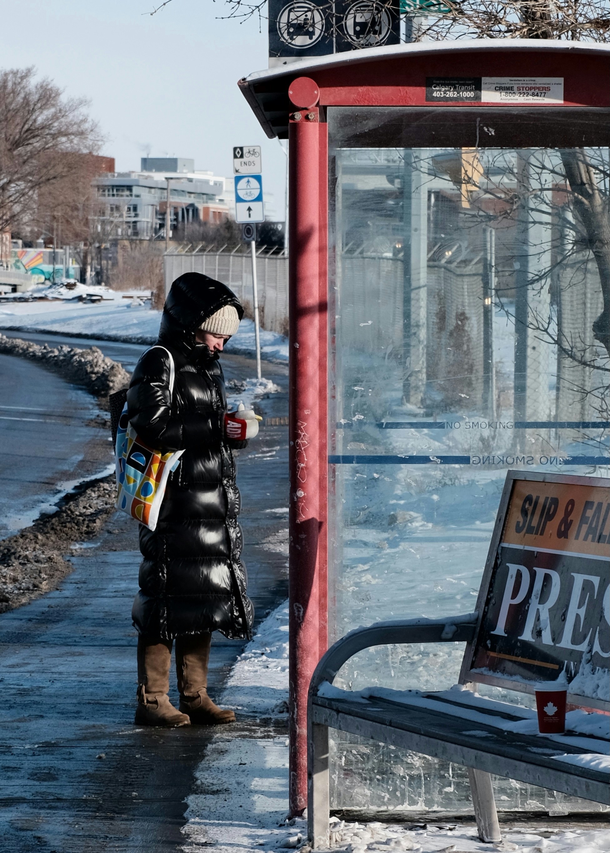A woman standing next to a bus stop on a snowy day