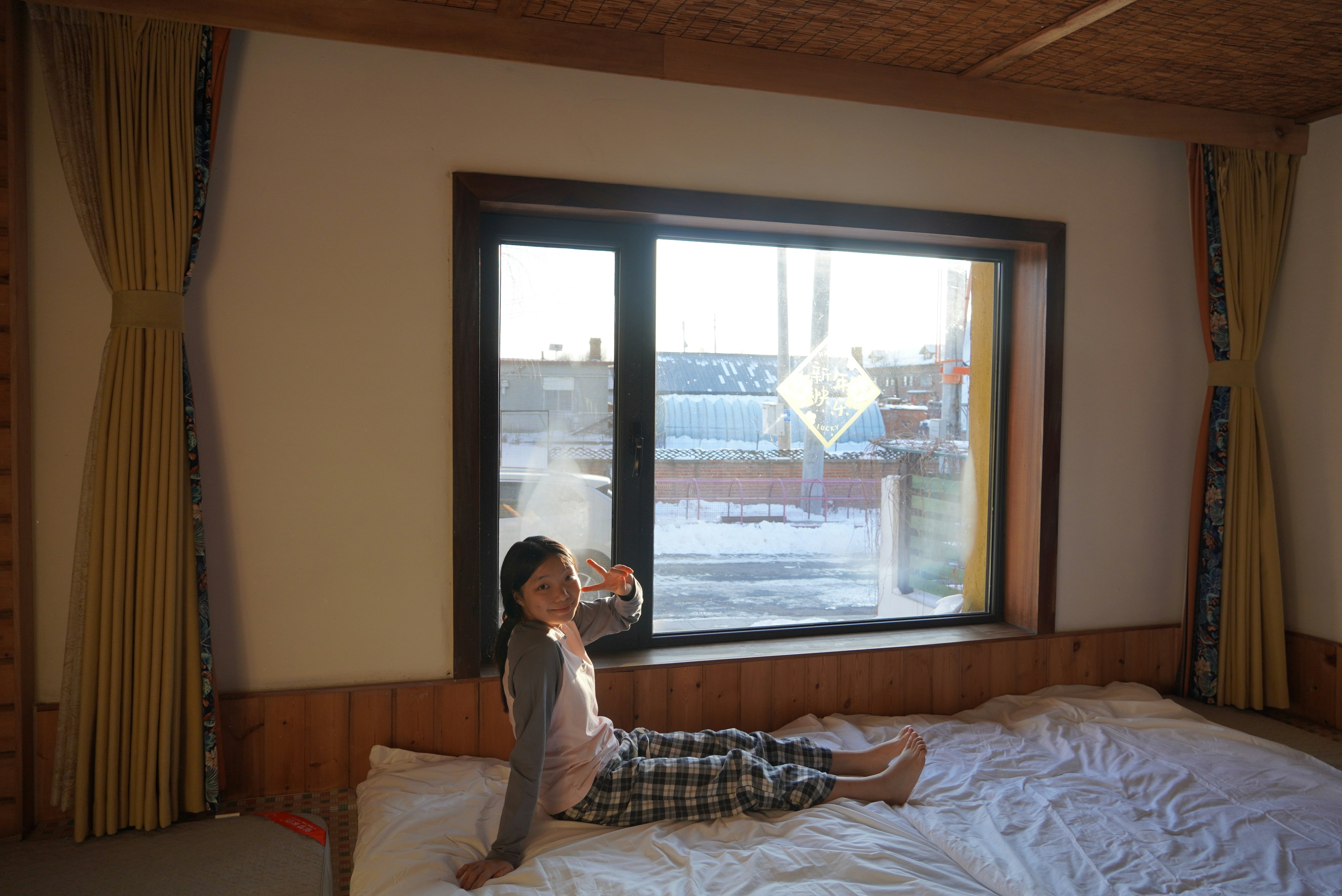 A little girl sitting on a bed in front of a window