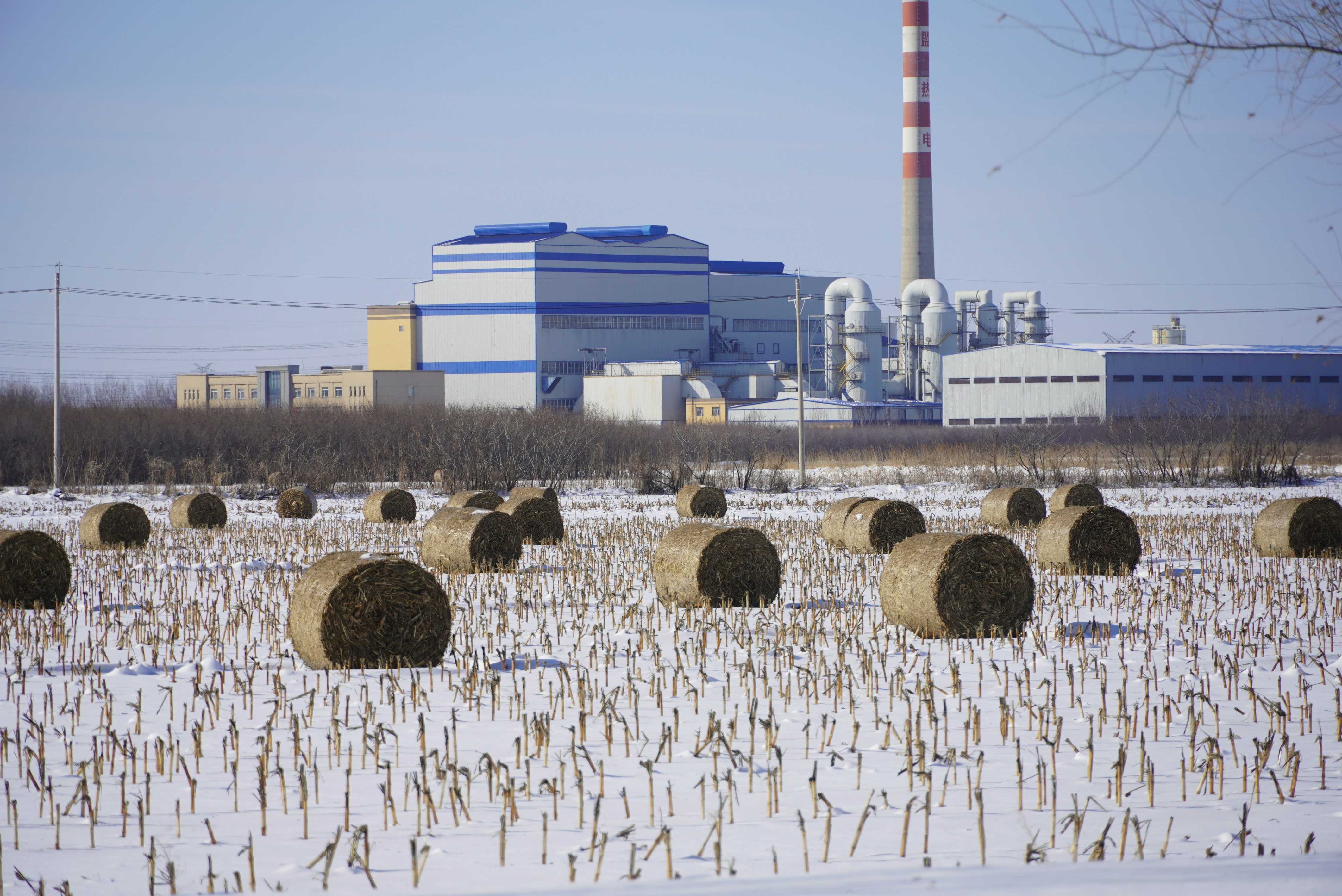 A large field of hay with a factory in the background