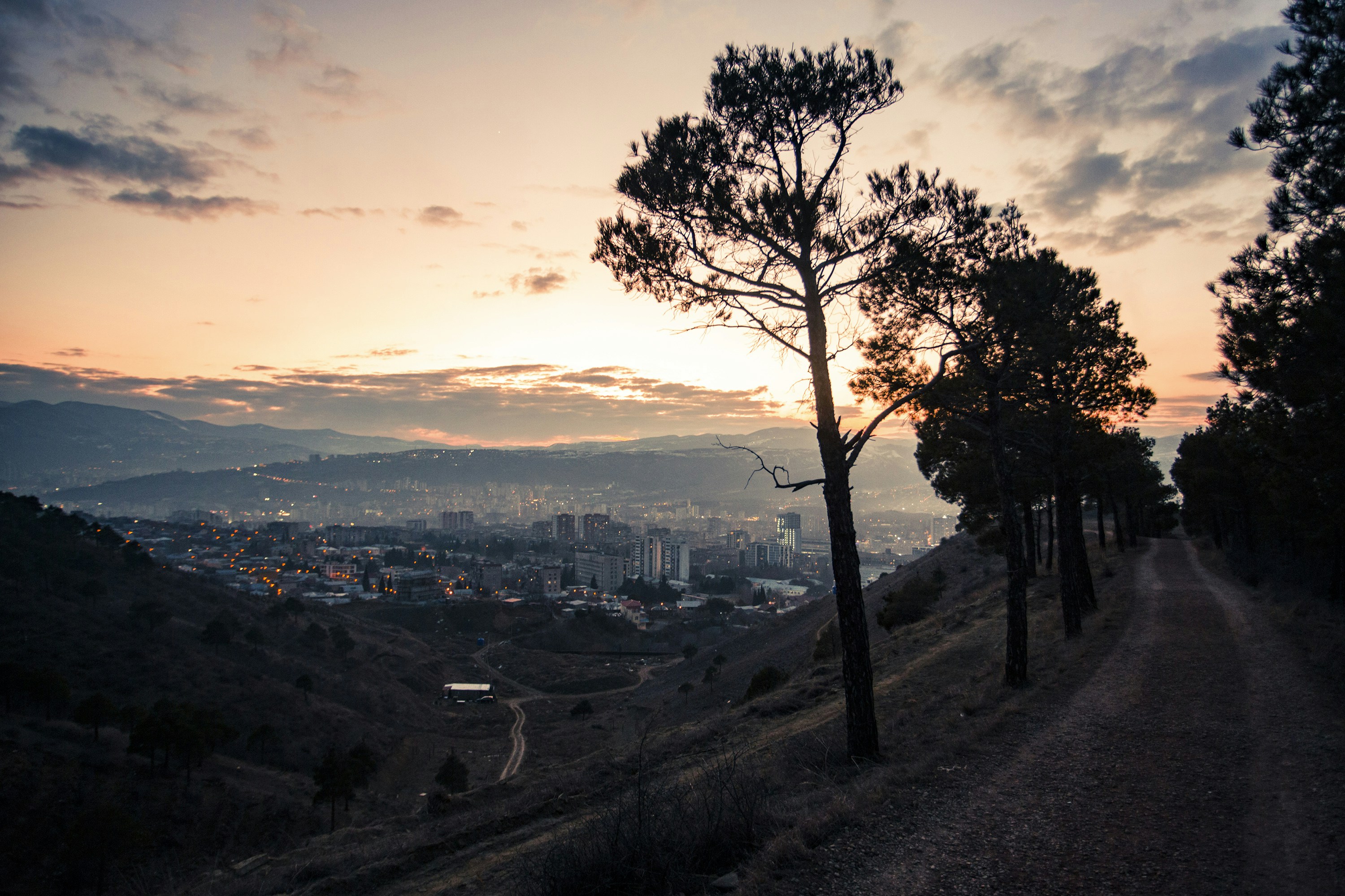 The sun is setting over the city from the top of a hill