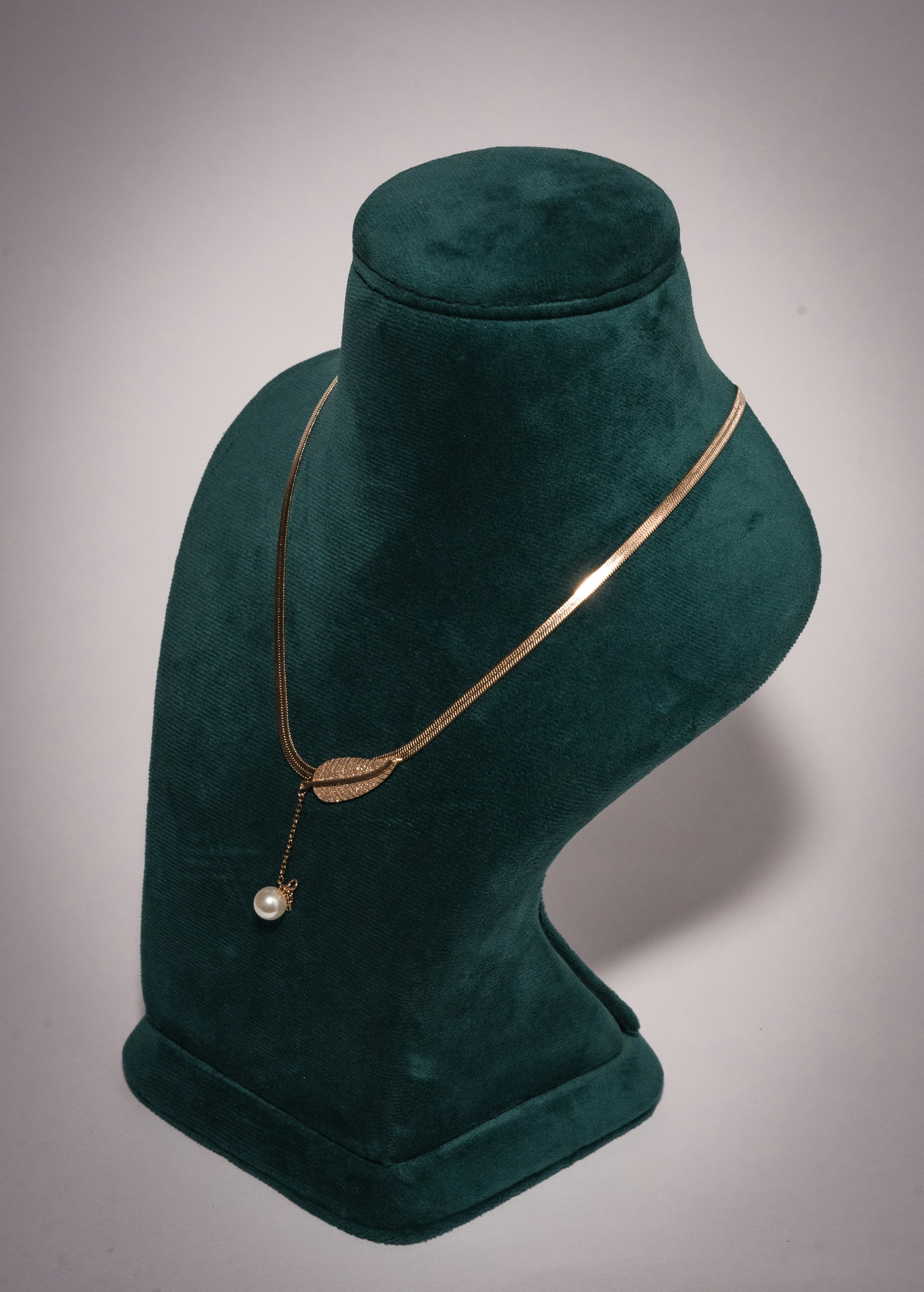 Gold leaf pendant necklace with a pearl on a display bust.