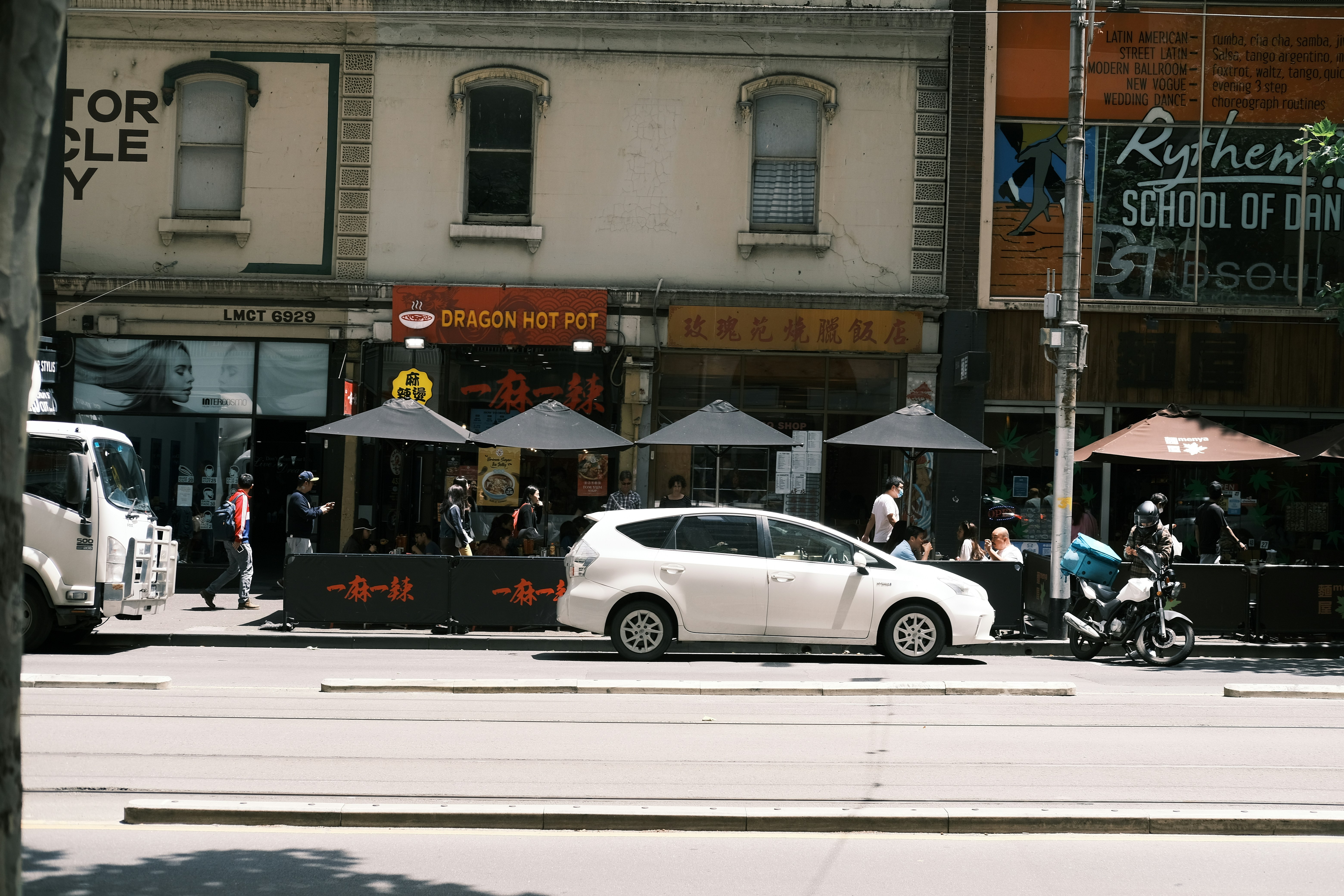 A white car driving down a street next to tall buildings