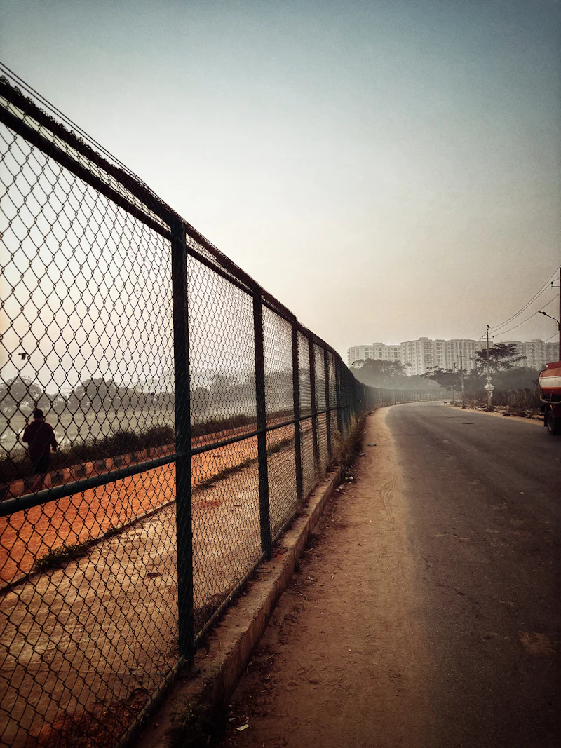 road stretching out at a distance with a fence on the left with haze and buildings at a distance