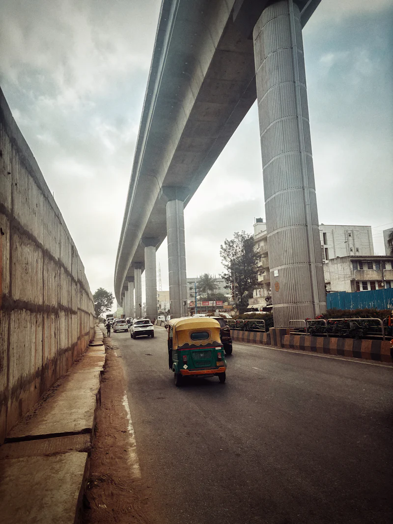 auto rickshaw on a road beneath elevated metro pillars