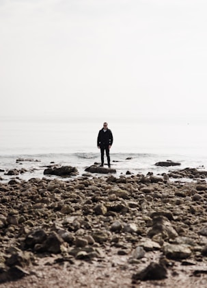 A man standing on a rocky beach next to the ocean