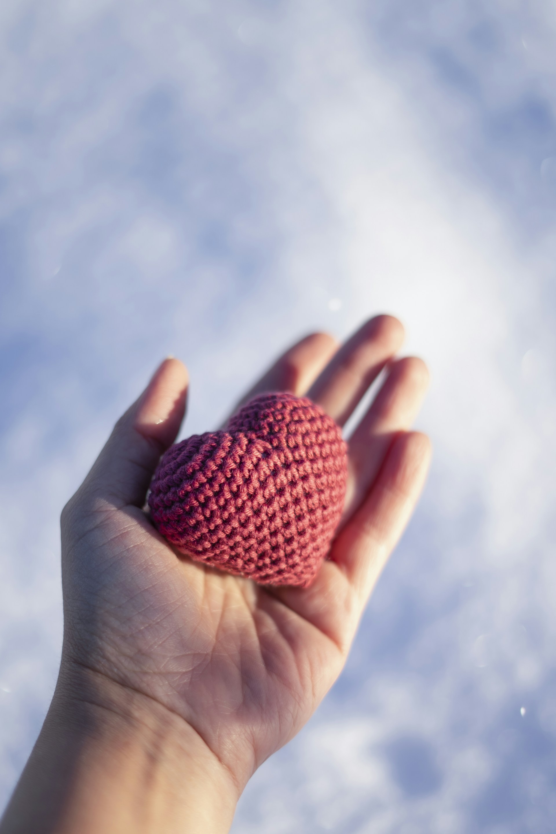 A hand holding a crocheted heart in the sky