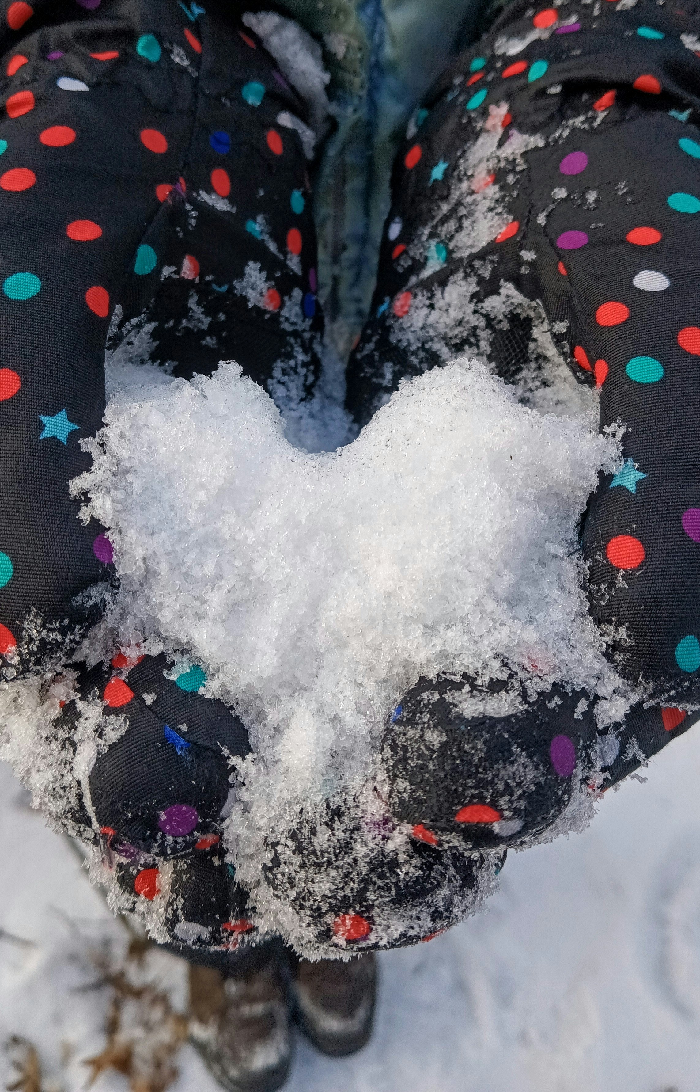 A person standing in the snow holding a heart shaped snowball