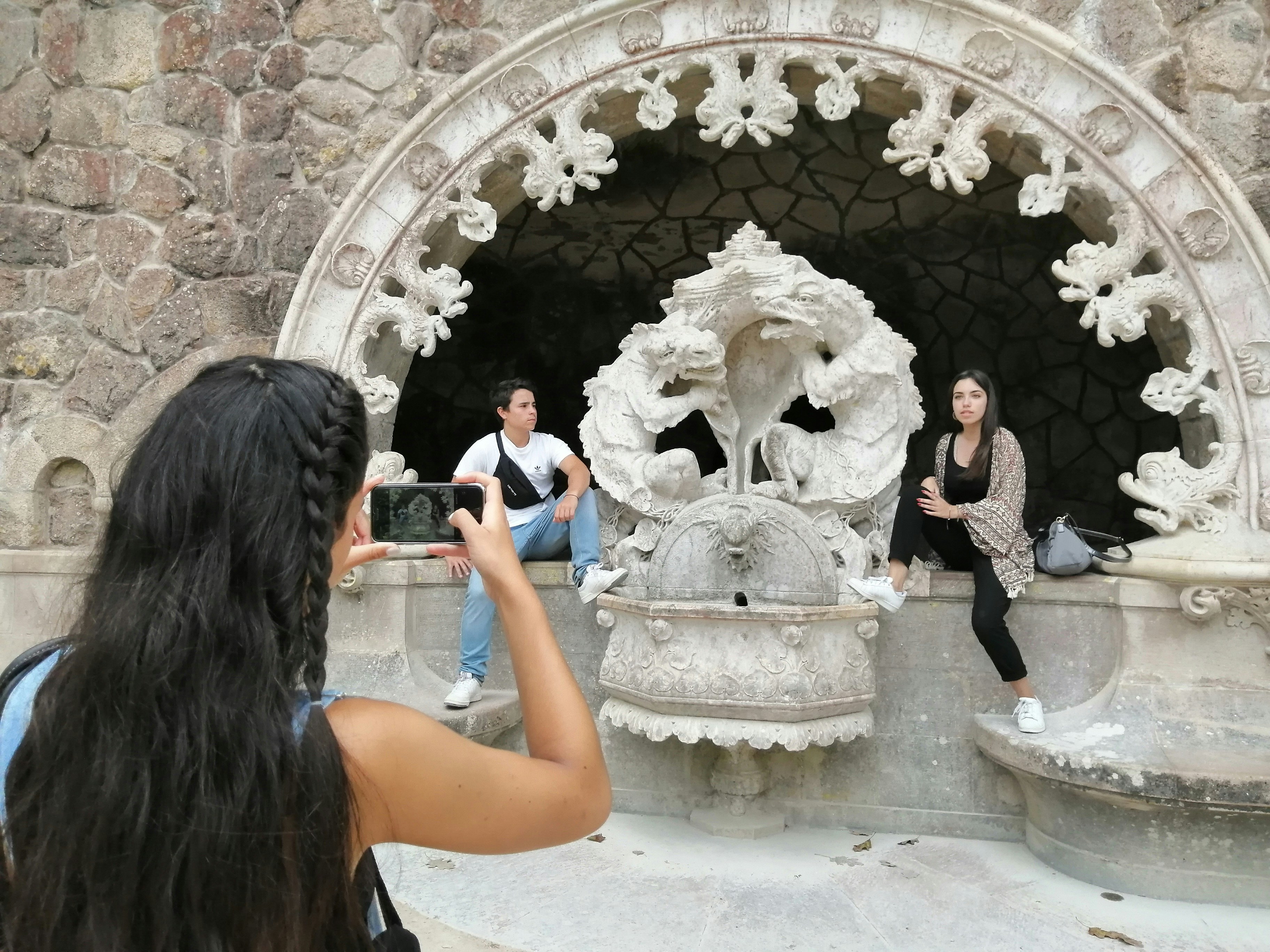 A woman taking a picture of a group of people in front of a fountain