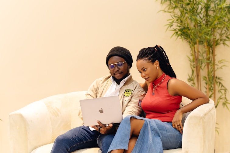 A man and a woman sitting on a couch looking at a laptop