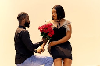 A man kneeling down next to a woman holding a bouquet of flowers