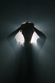 A man standing in the dark with his hands on his head