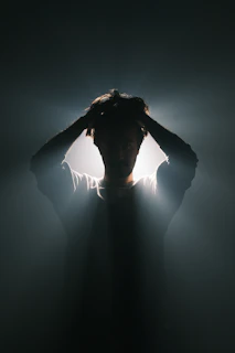 A man standing in the dark with his hands on his head