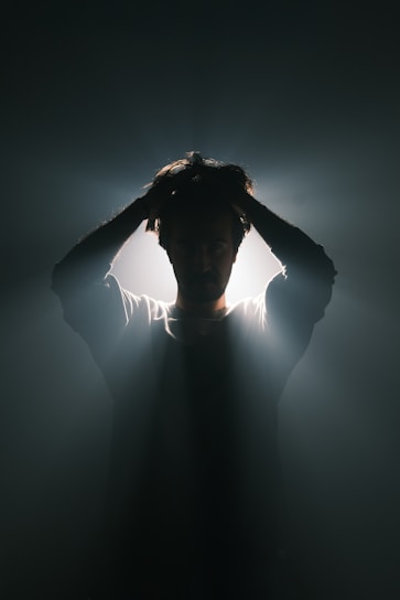 A man standing in the dark with his hands on his head