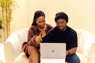A man and a woman sitting on a couch looking at a laptop