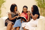 Three women sitting on a couch reading a book