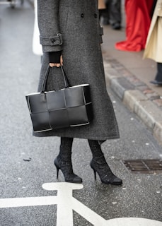 A woman in a gray coat is holding a black bag