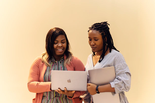 A couple of women standing next to each other with laptops