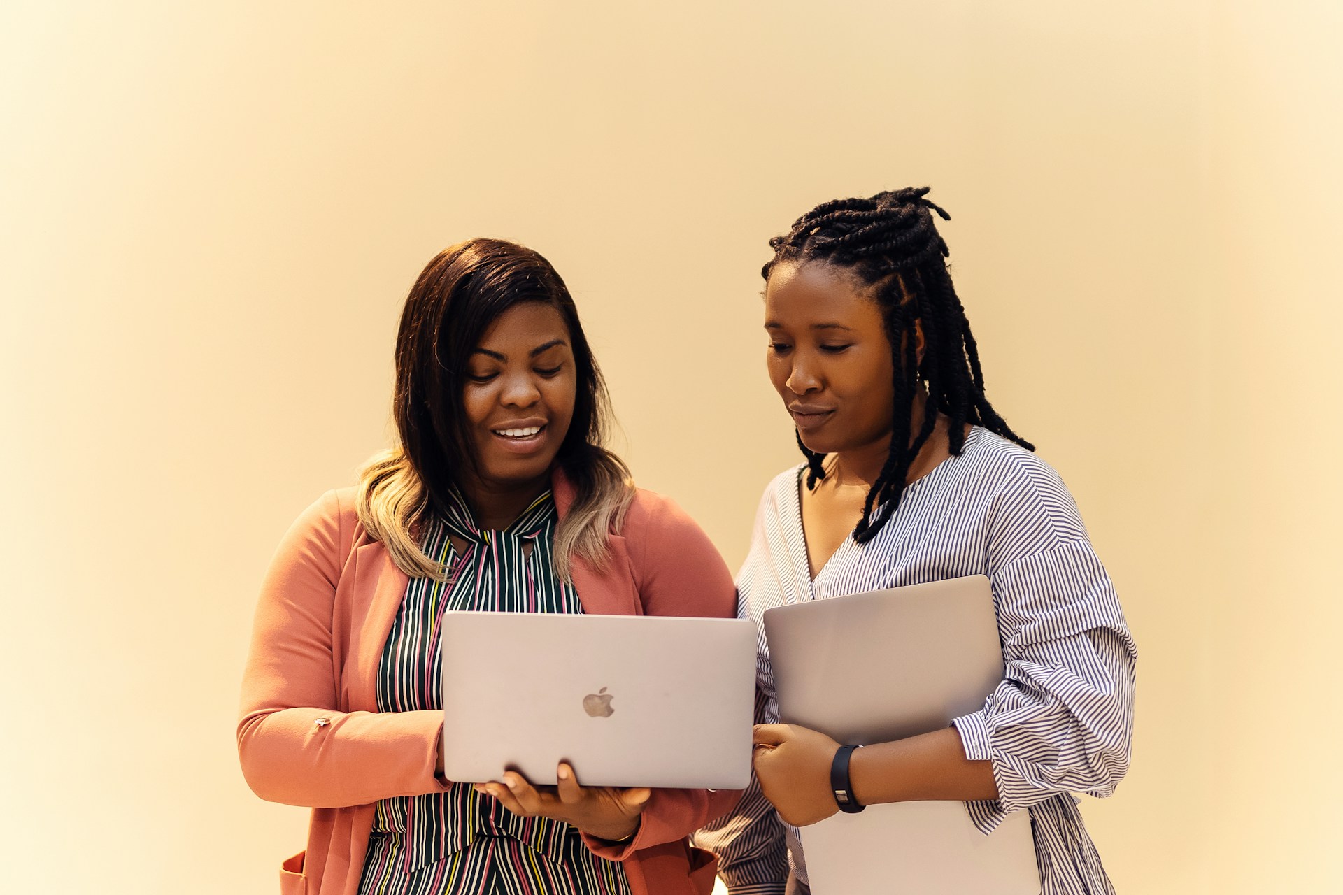 A couple of women standing next to each other with laptops