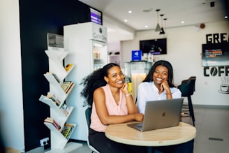 Two women sitting at a table with a laptop