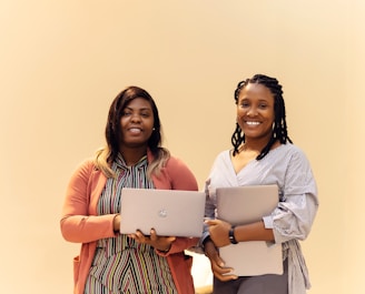 Two women standing next to each other holding laptops