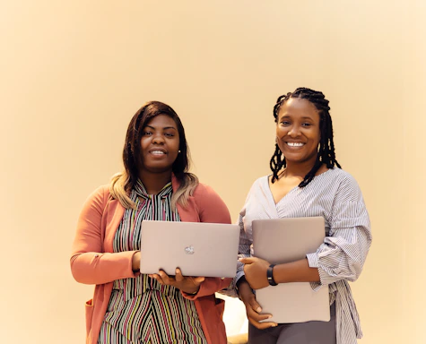 Two women standing next to each other holding laptops