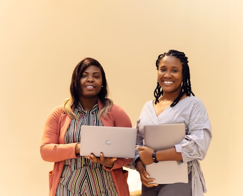 Two women standing next to each other holding laptops