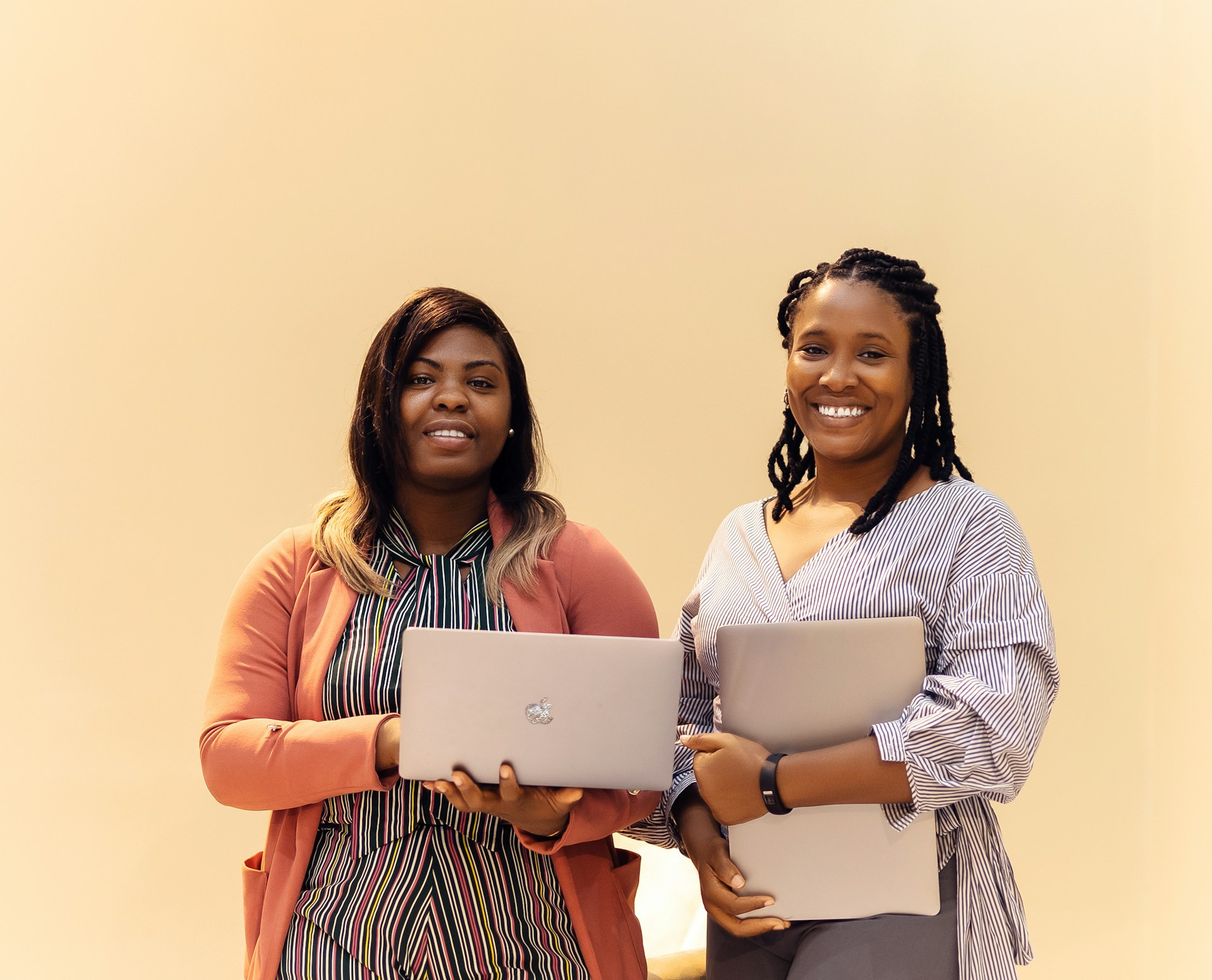 Two women standing next to each other holding laptops
