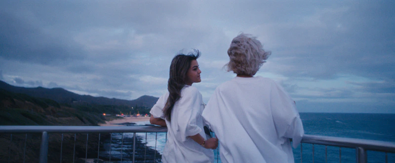 Sugar Mommy y Sugar Baby en un balcón con vista al océano.