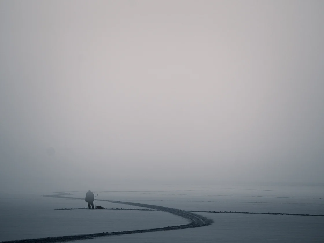 A solitary figure stands in the middle of a vast, fog-shrouded field, embodying the quiet power of the individual against an immense and uncertain landscape