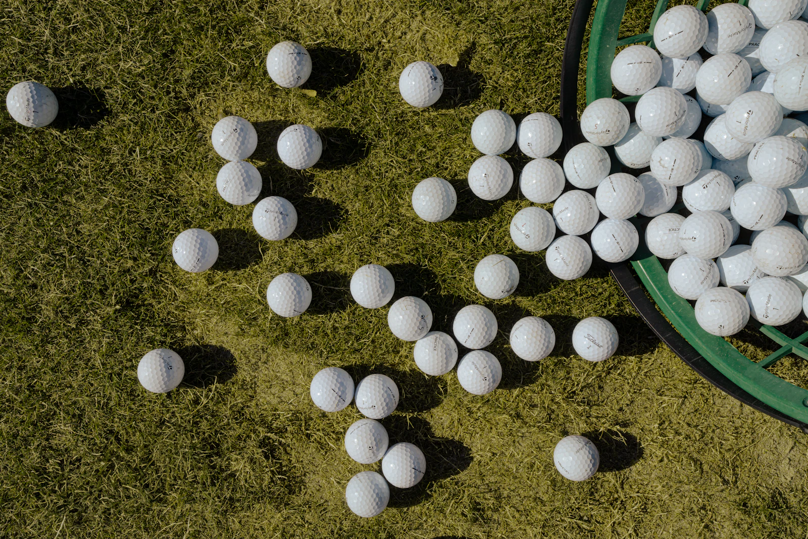 White range golf balls scattered on the grass beside a basket