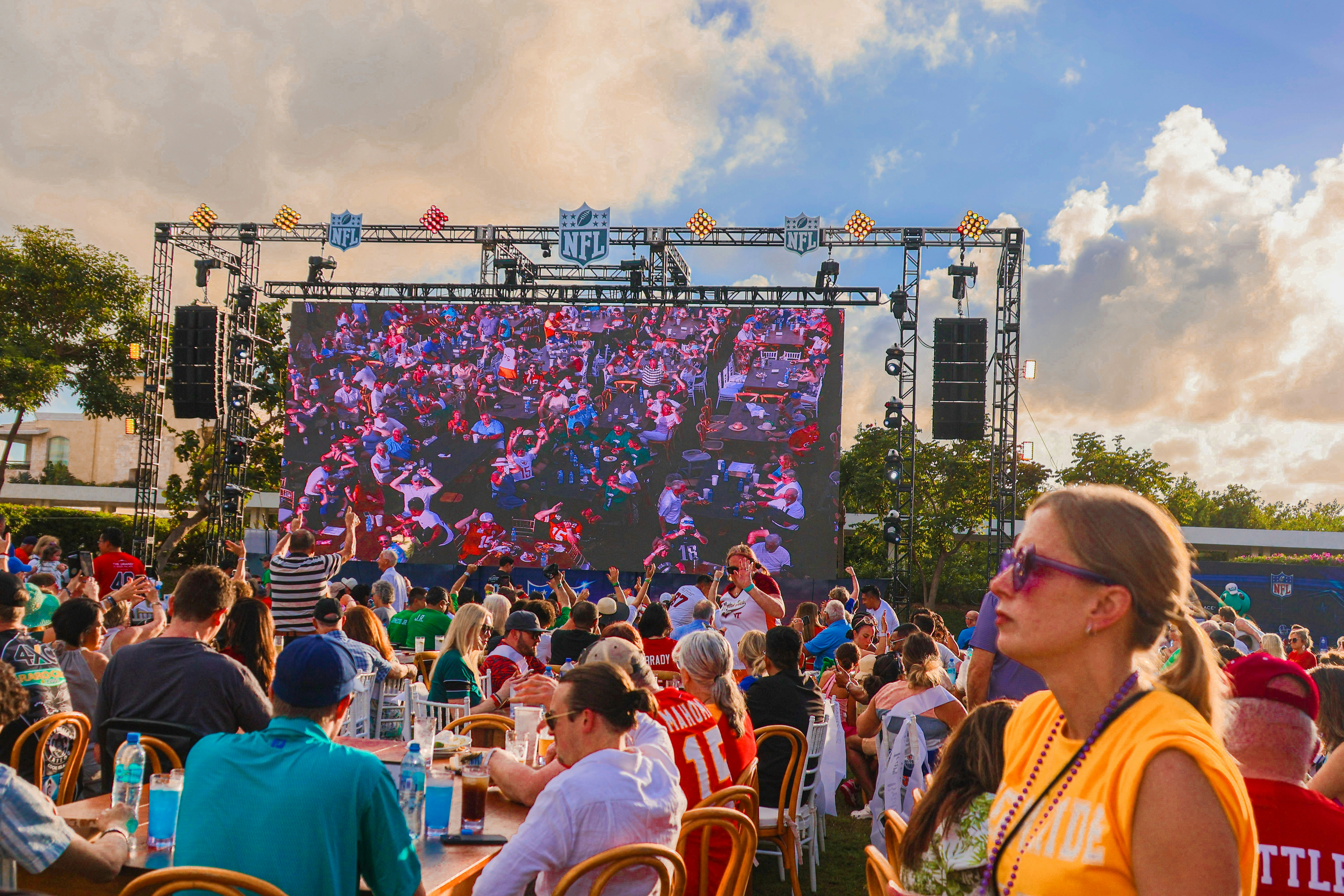 Crowded outdoor Super Bowl watch party with fans gathered around a large screen