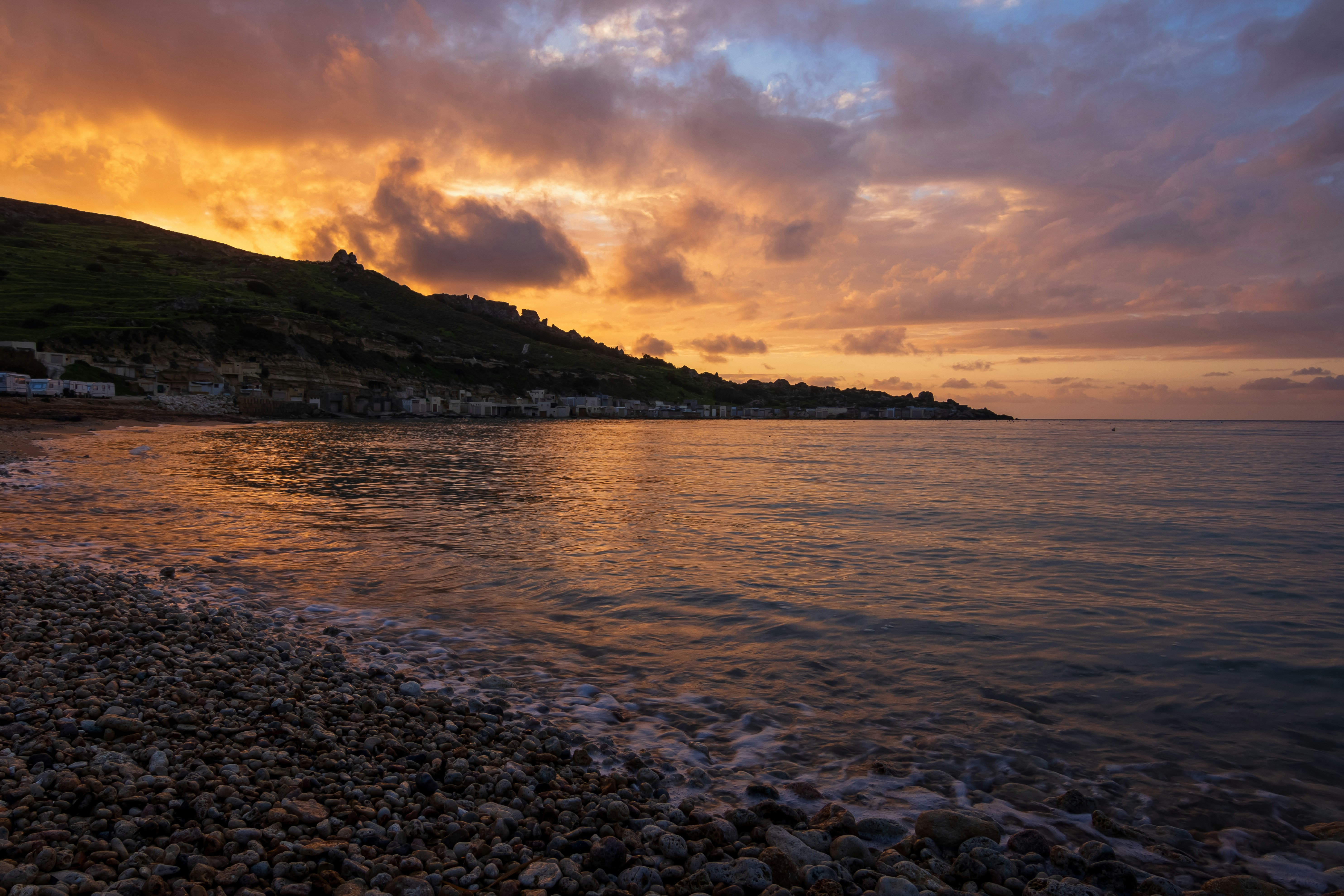 A sunset over a rocky beach with a hill in the background