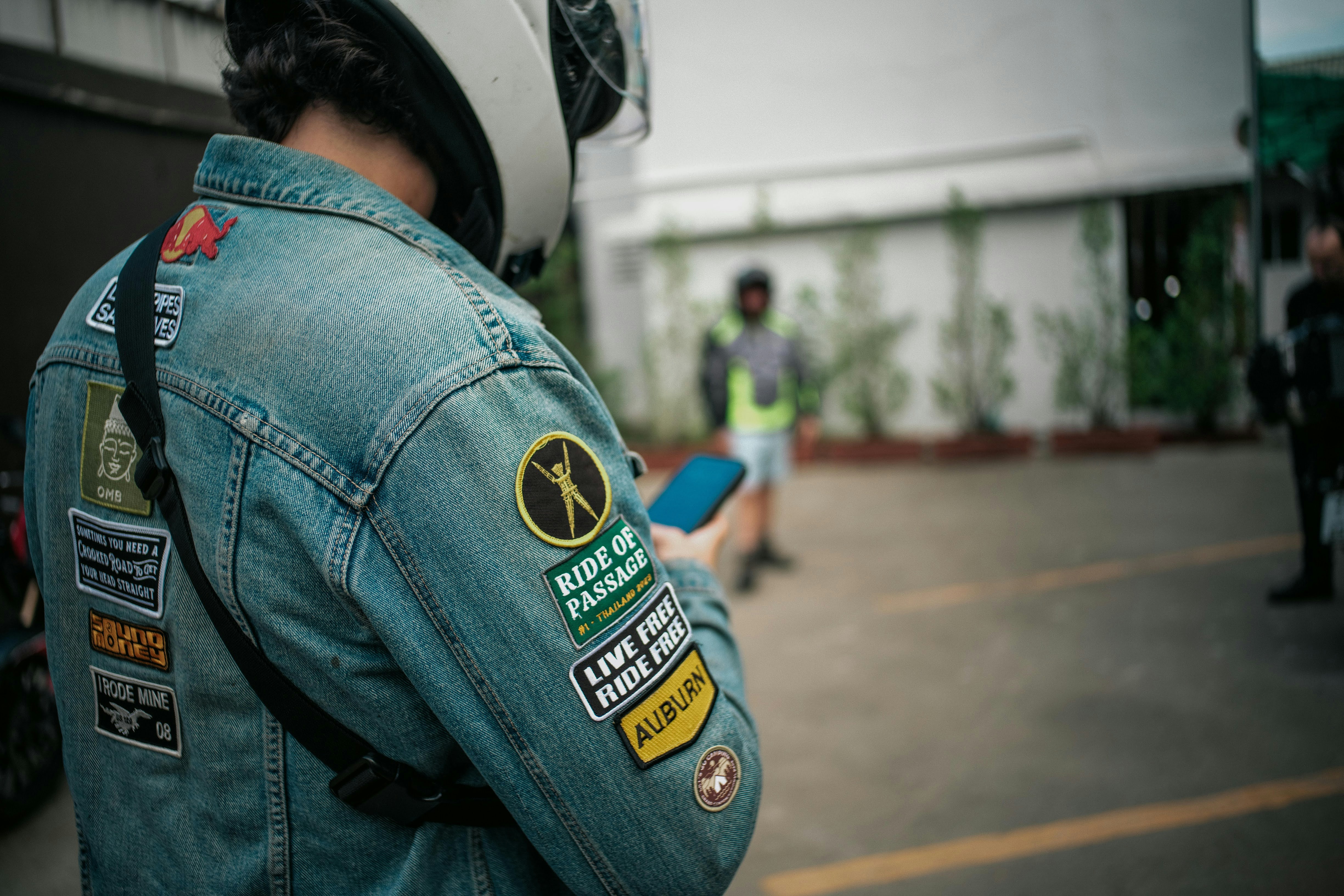 A man in a jean jacket and helmet standing in a parking lot