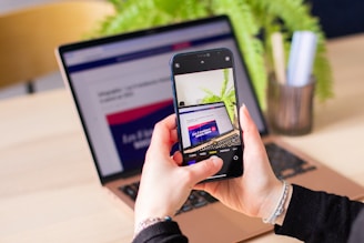 A person holding a cell phone in front of a laptop