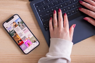 A woman typing on a laptop computer next to a cell phone