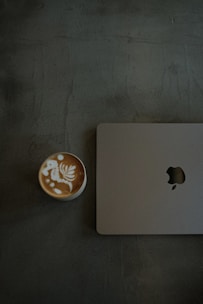 A cup of coffee sitting next to an apple laptop