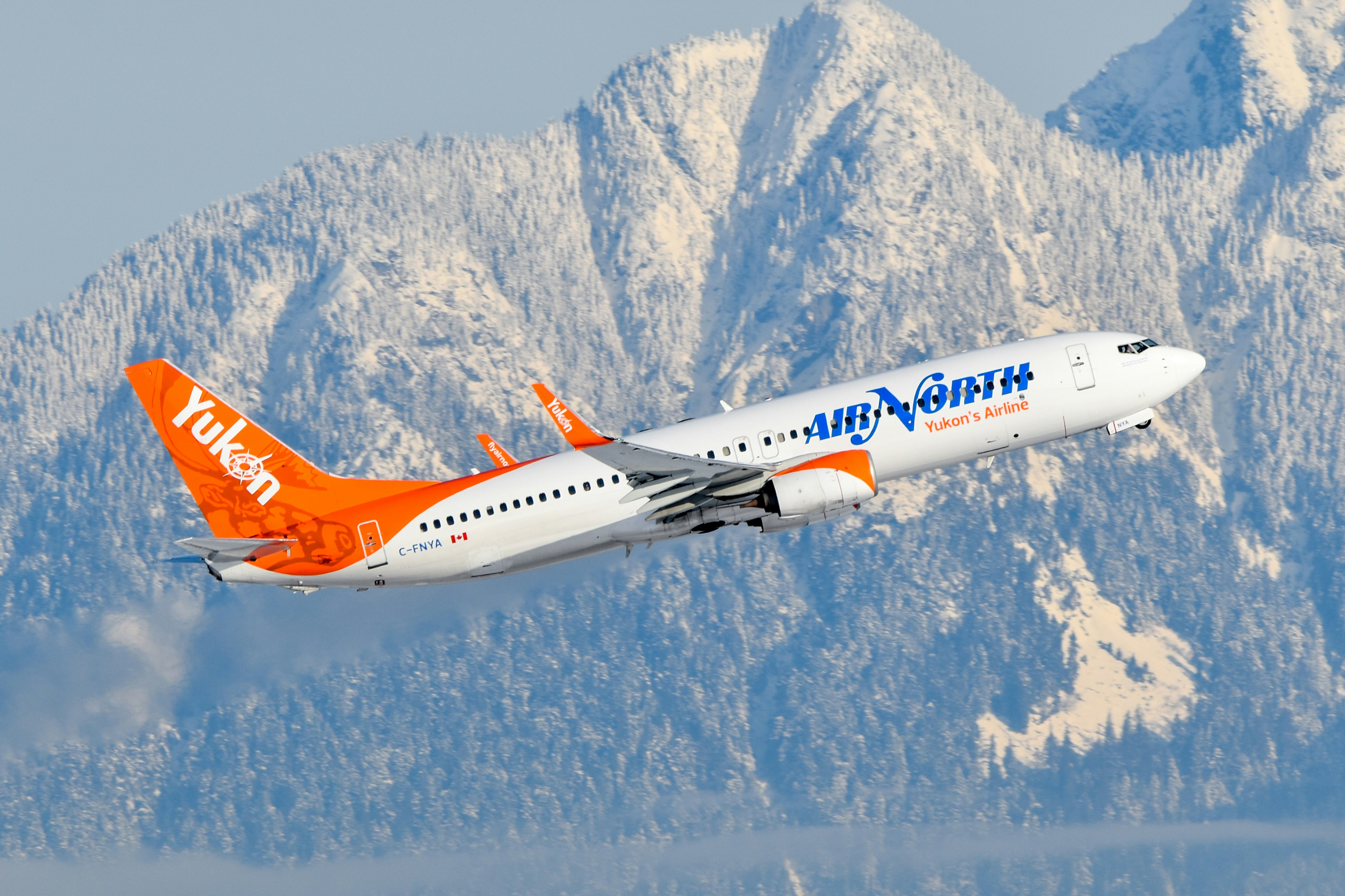 An orange and white airplane flying over a mountain range, Air North 737 departing Vancouver