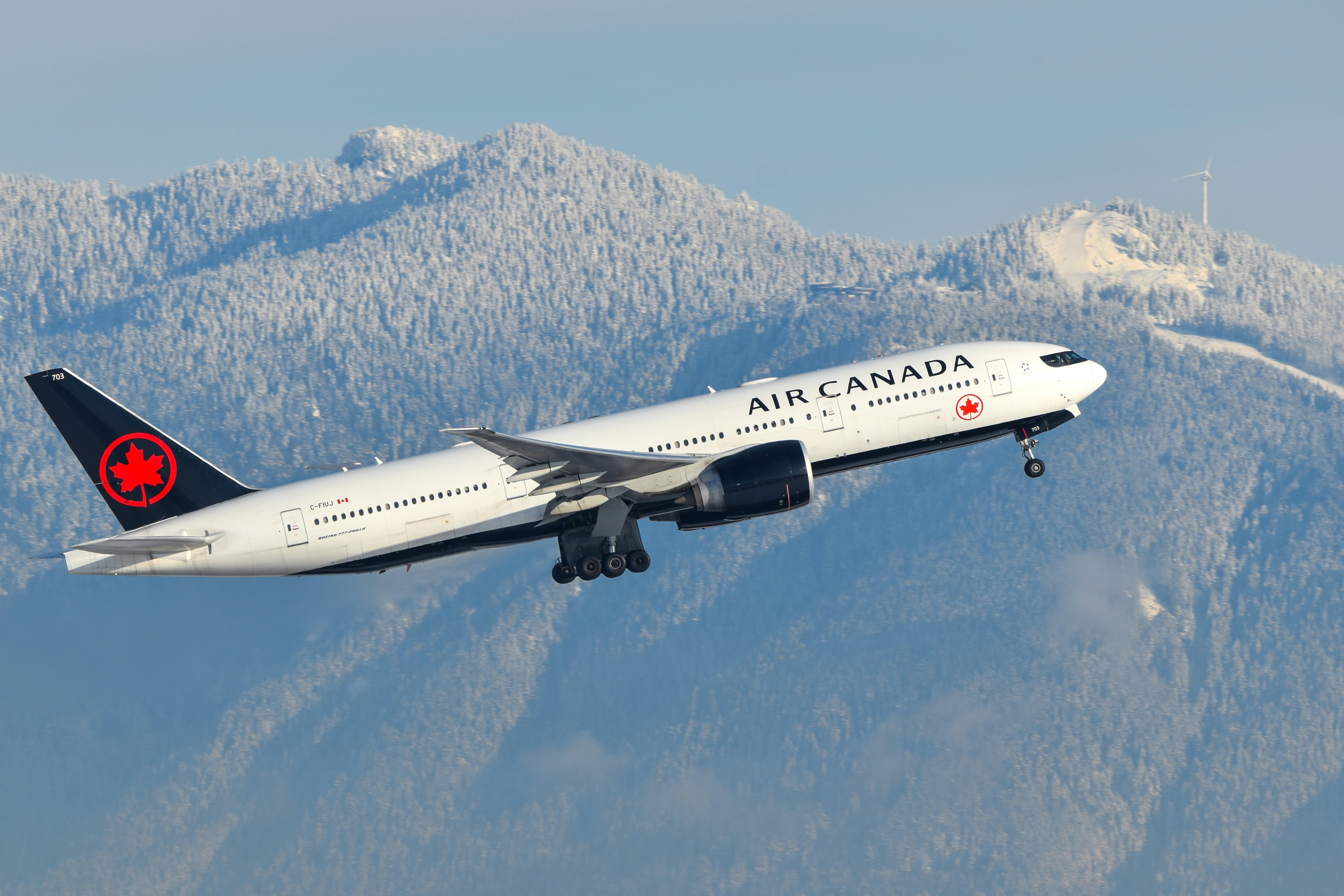A large jetliner flying over a mountain covered in snow, Air Canada 777 departing Vancouver