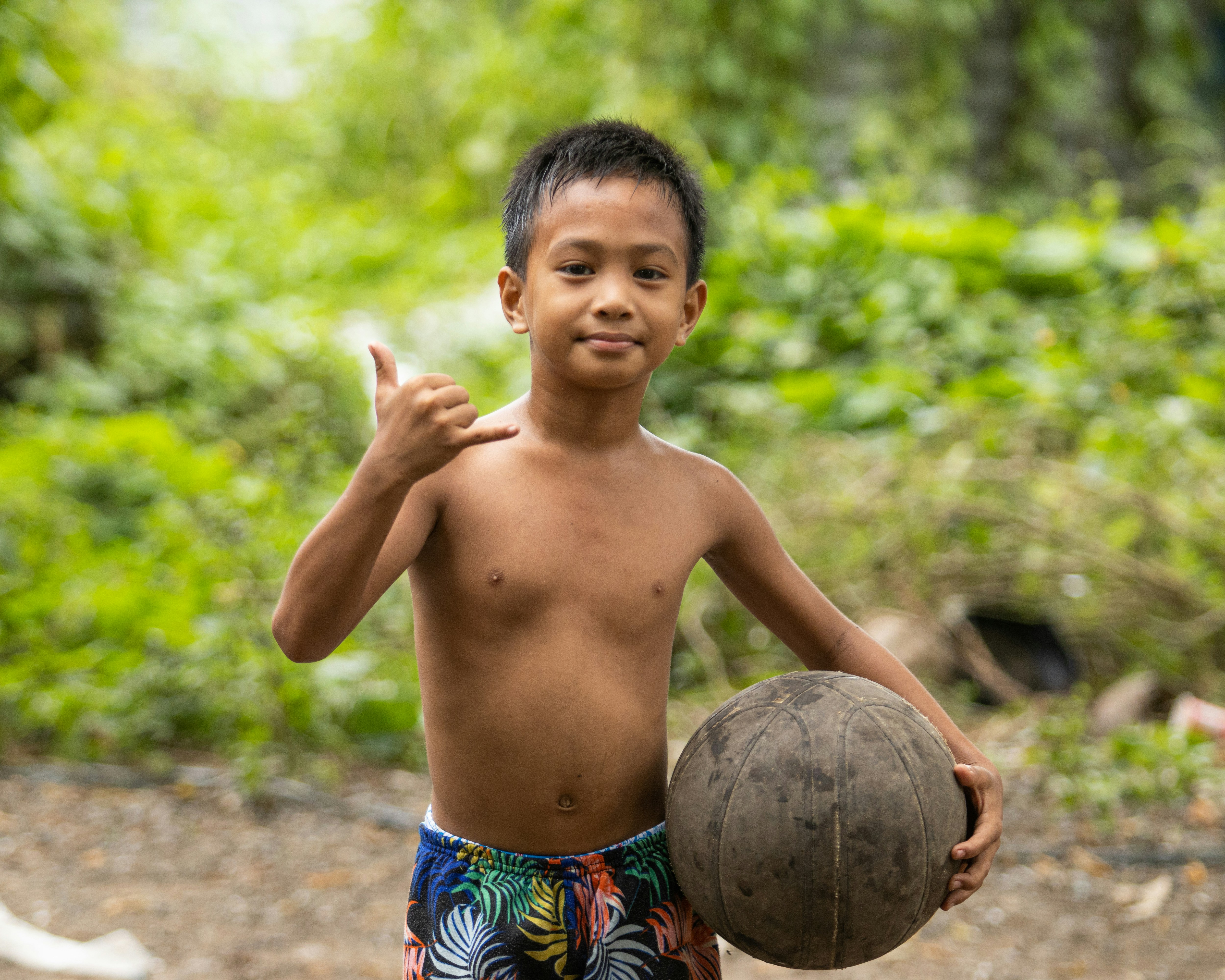 A young boy holding a ball and giving a thumbs up