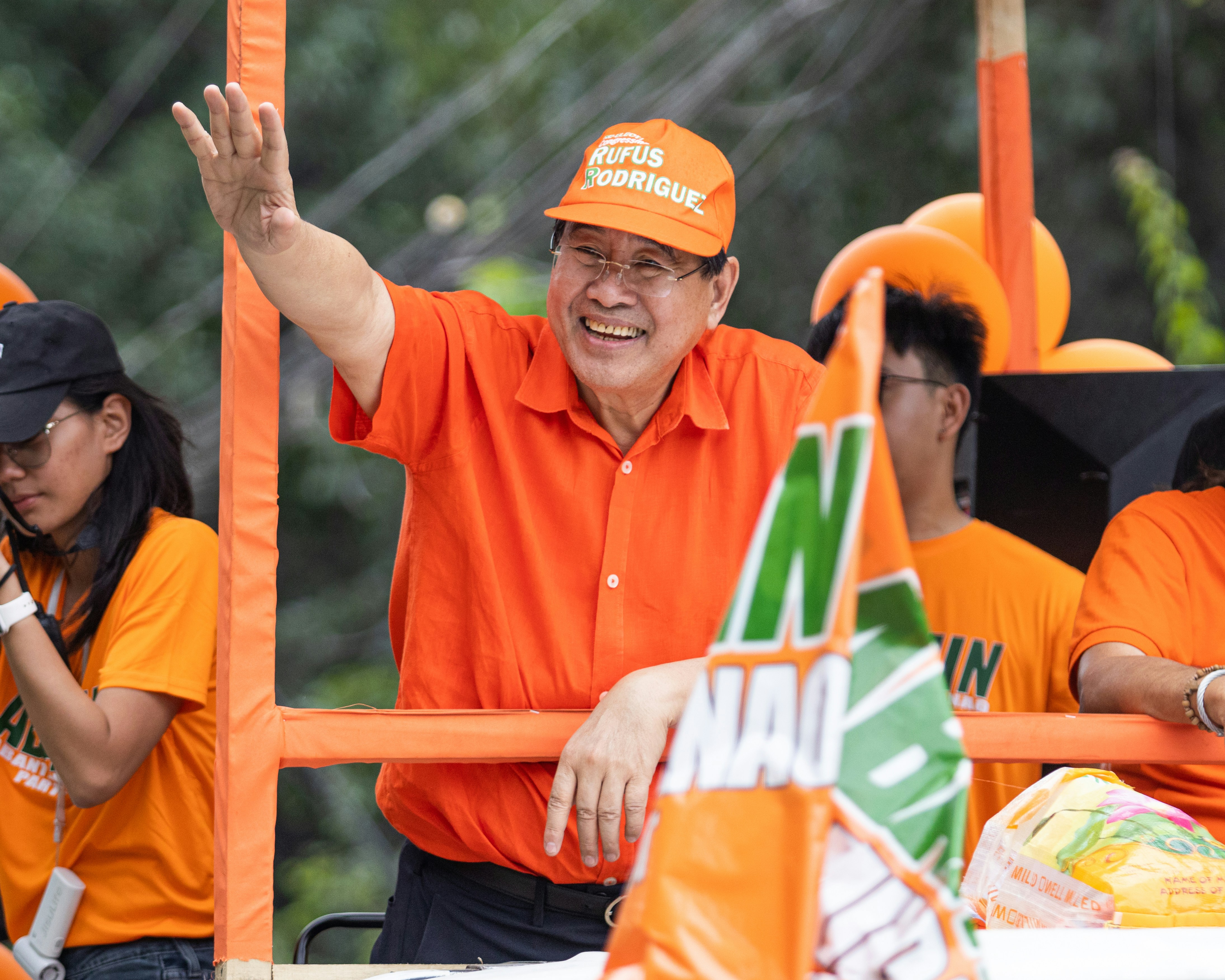 Politician in an orange shirt waves from a campaign float.
